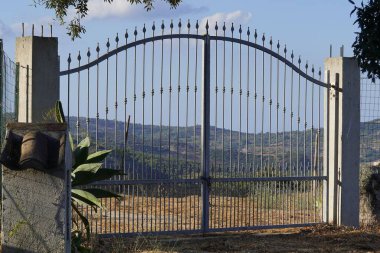 Titreyen tepeleri olan sakin bir İtalyan kırsalı tarafından galvanize edilmiş ve çerçevelenmiş klasik bir demir kapı, barışı koruyor gibi görünüyor..