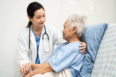 Asyalı doktor yaşlı kadın hasta sağlığını hastanede kontrol edip tedavi ediyor.
