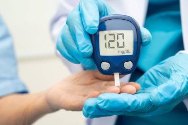 Diyabet tedavisinde kan şekeri seviyesini kontrol etmek için dijital glikoz ölçer kullanan Asyalı doktor.