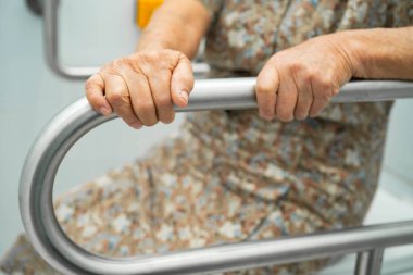 Asyalı yaşlı kadın hasta tuvaletteki destek parmaklıklarında tırabzan emniyeti kullanıyor..