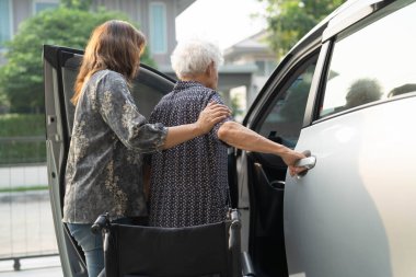 Bakıcı, Asyalı yaşlı kadın maluliyet hastasının arabasına binmesine yardım ediyor..