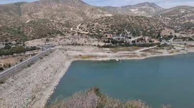 Kıbrıs 'ın dolambaçlı bir dağ yolu ile çevrili bir rezervuarın yer aldığı güzel bir hava görüntüsü. Çevresindeki manzarada engebeli tepeler ve dağınık evler doğal güzelliği ve suyu gözler önüne seriyor.