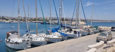 Bir dizi yelkenli ve yat, güneşli bir günde Kıbrıs Rum Kesimi 'ndeki bir marinanın iskelesine yanaştı. Sakin mavi su, berrak gökyüzü ve uzak kasaba davetkar bir deniz atmosferi yaratır, mükemmel.