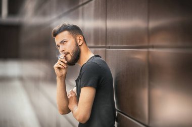 Bir genç yakışıklı beyaz sakallı adam siyah t-shirt ilkbaharda sokakta sigara içiyor. Yakın çekim.