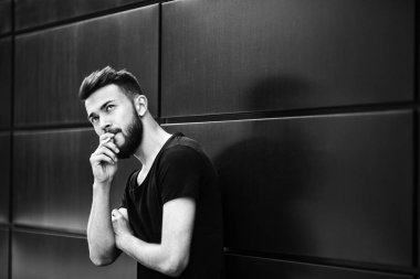 Bir genç yakışıklı beyaz sakallı adam siyah t-shirt ilkbaharda sokakta sigara içiyor. Yakın çekim. Siyah ve beyaz.