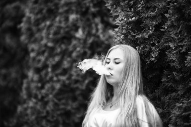 Vape genç. Bir genç Sevimli beyaz bir elbise vaping sokakta elektronik sigara yaz aylarında kızıdır. Siyah ve beyaz.