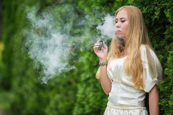 Vape genç. Bir genç Sevimli beyaz bir elbise vaping yaz aylarında sokakta mazı arasında elektronik sigara kızıdır.