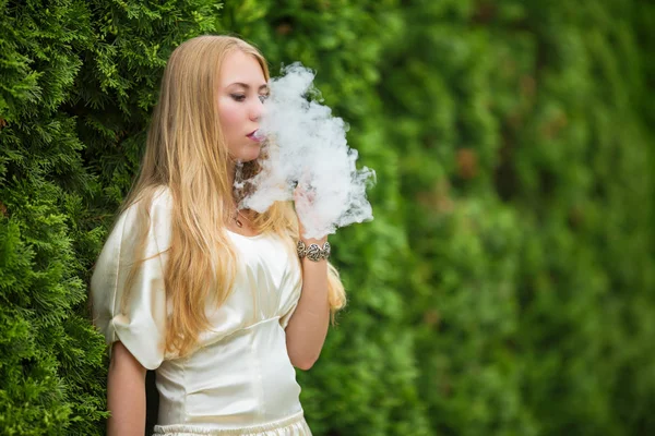 Vape genç. Bir genç Sevimli beyaz bir elbise vaping yaz aylarında sokakta mazı arasında elektronik sigara kızıdır.