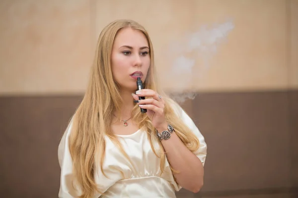 Vape 一个年轻可爱的白色女孩穿着连衣裙是 Vaping 一根电子香烟对面的墙上的街道上的夏天 — 图库照片