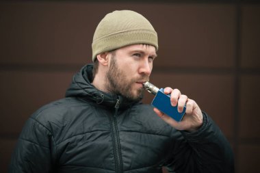 Vape adam. Genç sakallı kap beyaz adam ve siyah ceket elektronik sigara sigara modern karşısında