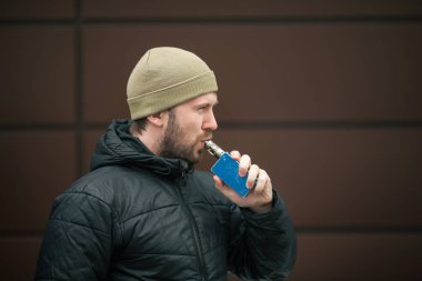 Vape adam. Genç sakallı kap beyaz adam ve siyah ceket elektronik sigara sigara modern karşısında