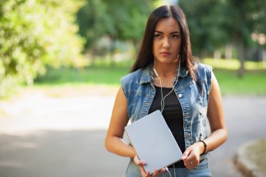 Genç güzel esmer kız tablet ve yaz aylarında sokakta müzik dinlemek.