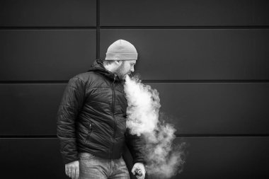 Vape adam. Genç sakallı beyaz şapkalı adam bir elektronik sigara ve buhar icar. Kötü alışkanlık. Siyah ve beyaz.