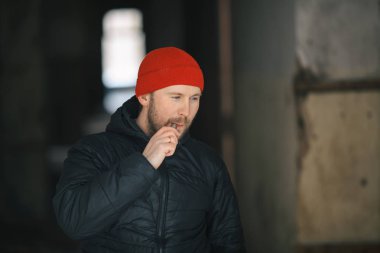 Vape hayatta. Genç adam kırmızı şapkalı beyaz ve siyah ceket harap bir ev koridorda elektronik sigara sigara içiyor.