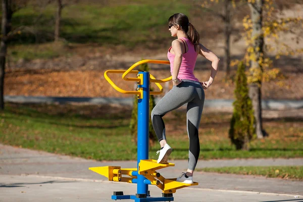 サングラスでスポーツ少女は秋に公園でストリートのプレイ グラウンドでスポーツのシミュレータの横に立っています — ストック写真