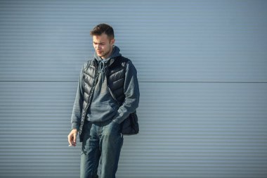 Siyah yelek bir genç yakışıklı adam ilkbaharda sokakta bir metal kapı önünde sigara içiyorum.