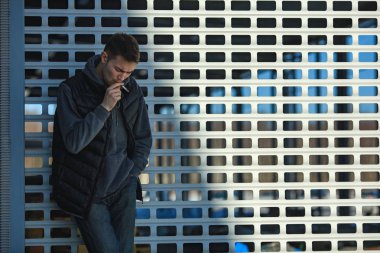 Siyah yelek bir genç yakışıklı adam ilkbaharda sokakta bir metal kapı önünde sigara içiyorum.