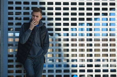 Siyah yelek bir genç yakışıklı adam ilkbaharda sokakta bir metal kapı önünde sigara içiyorum.