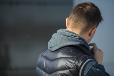 Siyah yelek genç bir adam bize sırtını duran ve ilkbaharda sokakta bir metal kapı önünde bir sigara.