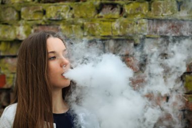 Vape genç. Genç güzel beyaz hırka baharda yıkılan tuğla duvar sokak karşısında elektronik sigara sigara içinde beyaz kız. Kötü alışkanlık.