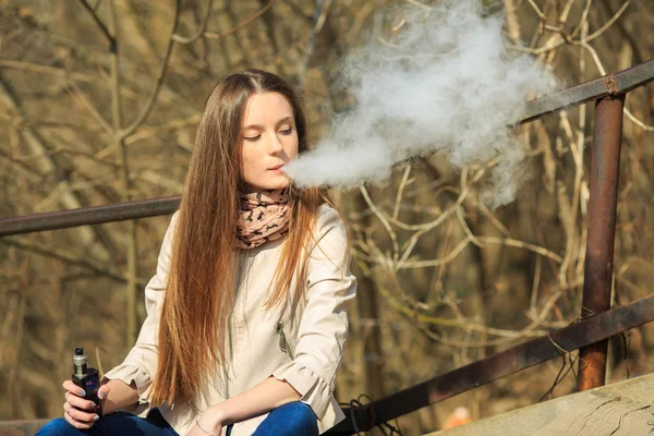 Vape genç. Gündelik giyim genç güzel beyaz kız bahar sokakta eski ahşap merdivenler üzerinde elektronik sigara sigara. Kötü alışkanlık. Vaping aktivitesi.