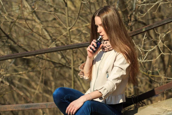 Vape genç. Gündelik giyim genç güzel beyaz kız bahar sokakta eski ahşap merdivenler üzerinde elektronik sigara sigara. Kötü alışkanlık. Vaping aktivitesi.