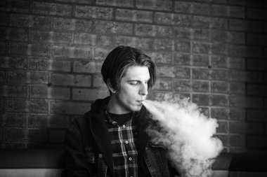 Vape genç. Barda elektronik sigara içen genç yakışıklı adamın portresi. Sağlık için zararlı kötü alışkanlık. Vaping aktivitesi. Siyah nad beyaz.