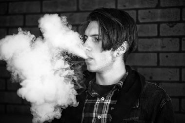 Vape genç. Barda elektronik sigara içen genç yakışıklı adamın portresi. Sağlık için zararlı kötü alışkanlık. Vaping aktivitesi. Siyah nad beyaz.