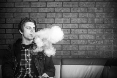 Vape genç. Barda elektronik sigara içen genç yakışıklı adamın portresi. Sağlık için zararlı kötü alışkanlık. Vaping aktivitesi. Siyah nad beyaz.