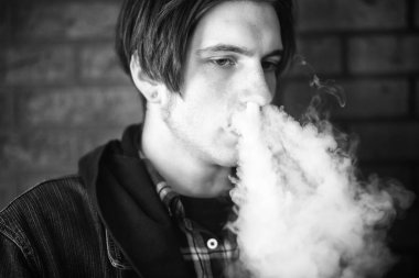Vape genç. Barda elektronik sigara içen genç yakışıklı adamın portresi. Sağlık için zararlı kötü alışkanlık. Vaping aktivitesi. Siyah nad beyaz. Yakın çekim.