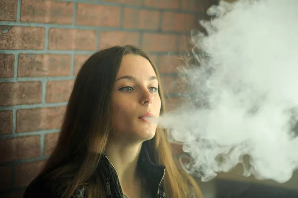 Vape teenager with  problem skin. Portrait of young cute girl in sunglasses smoking an electronic cigarette in the bar. Bad habit that is harmful to health. Vaping activity.