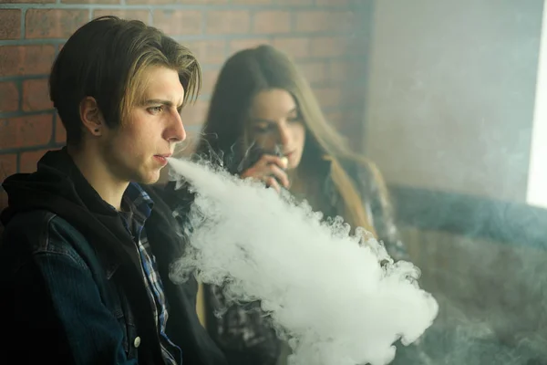 Vape gençleri. Güneş gözlüğü genç sevimli kız ve genç yakışıklı adam vape barda bir elektronik sigara duman. Sağlık için zararlı kötü alışkanlık. Vaping etkinliği.