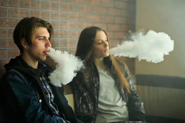 Vape gençleri. Güneş gözlüğü genç sevimli kız ve genç yakışıklı adam vape barda bir elektronik sigara duman. Sağlık için zararlı kötü alışkanlık. Vaping etkinliği.