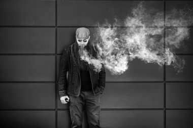 Vape sakallı adam. Bir şapka ve güneş gözlüğü çok uzun sakallı yetişkin bir adam güneşli bir gün dışında elektronik sigara içiyor. Sağlık için zararlı kötü alışkanlık. Siyah beyaz.