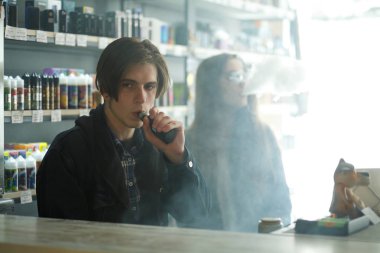 Vape gençleri. Genç yakışıklı adam ve güneş gözlüğü genç sevimli kız vape barda elektronik sigara duman. Sağlık için zararlı kötü alışkanlık. Vaping etkinliği.