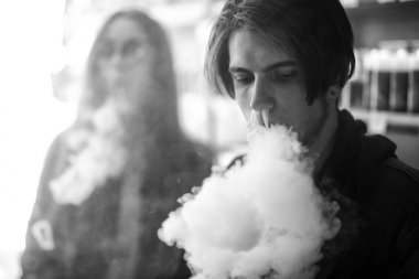 Vape gençleri. Genç yakışıklı adam ve güneş gözlüğü genç sevimli kız vape barda elektronik sigara duman. Sağlık için zararlı kötü alışkanlık. Vaping aktivitesi. Siyah ve beyaz. Yakın çekim.