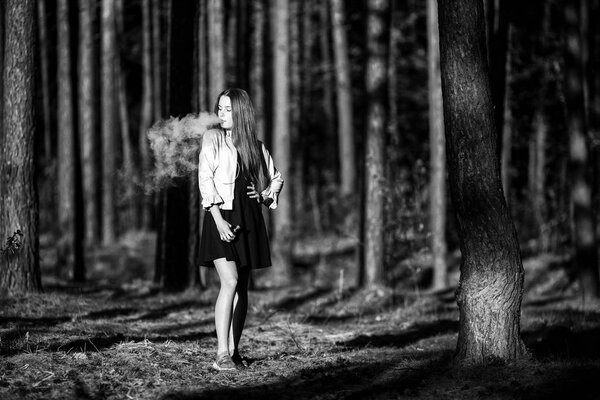 Vape teenager. Young cute girl in casual clothes smokes an electronic cigarette outdoors in the forest at sunset in summer. Bad habit that is harmful to health. Vaping activity. Black and white.