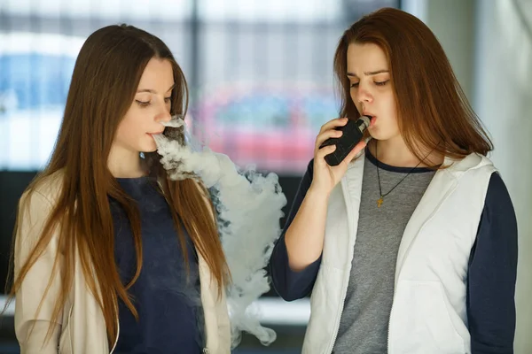 Vape gençleri. Gündelik giysiler içinde iki genç sevimli kız yaz günü sokakta elektronik sigara duman. Sağlık için zararlı kötü alışkanlık. Vaping etkinliği.