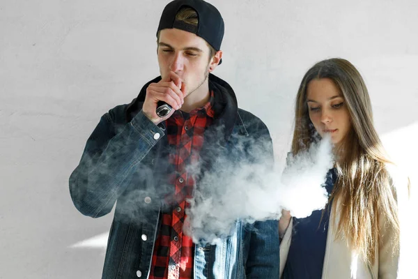 Vape genç. Rahat giysiler ve bir kap içinde yakışıklı adam genç sevimli kız açık havada bir elektronik sigara duman. Sağlık için zararlı kötü alışkanlık. Vaping etkinliği.