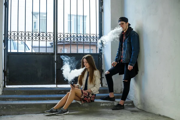 Vape genç. Rahat giysiler içinde genç sevimli kız ve bir kap yakışıklı adam hapishane hücresinde elektronik bir sigara duman. Sağlık için zararlı kötü alışkanlık. Vaping etkinliği.