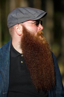 Sakallı adam. Ormanda güneşli bir günde şapkalı ve güneş gözlüklü çok uzun sakallı ciddi beyaz yetişkin bir adamın portresi. Yakın çekim.