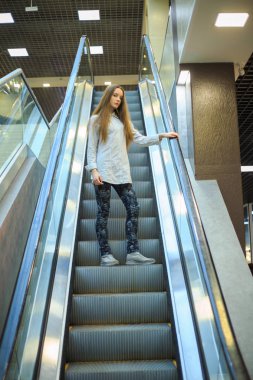 Bir alışveriş merkezinde yürüyen merdiven üzerinde bir gömlek uzun saçlı Genç bir güzel beyaz genç kız portre.