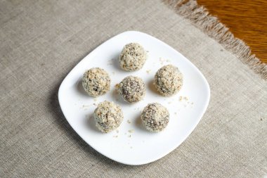 Masanın üzerinde keten peçete üzerinde beyaz bir tabak üzerinde kurutulmuş meyve ve ceviz topları şeklinde ev yapımı şeker. Şeker ve gluten olmadan sağlıklı gıda.