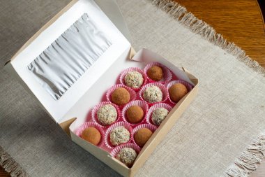 Masanın üzerinde keten peçete üzerinde kutuiçinde ceviz ve kakao tozu ile kurutulmuş meyve topları şeklinde ev yapımı şeker. Şeker ve gluten olmadan sağlıklı gıda.