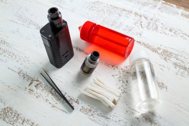 Vape nesneleri. Hafif ahşap bir masa üzerinde e-sıvı ile elektronik sigara ve kavanoz.