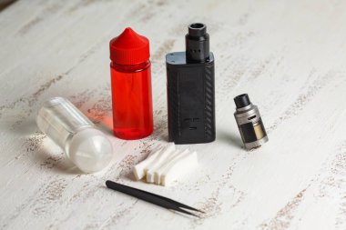 Vape nesneleri. Hafif ahşap bir masa üzerinde e-sıvı ile elektronik sigara ve kavanoz.