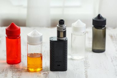 Vape nesneleri. Hafif ahşap bir masa üzerinde e-sıvı ile elektronik sigara ve kavanoz.