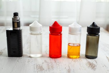 Vape nesneleri. Hafif ahşap bir masa üzerinde e-sıvı ile elektronik sigara ve kavanoz.