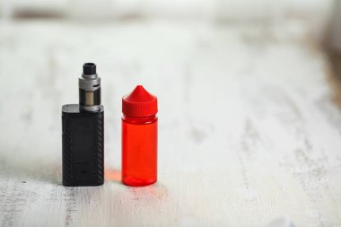 Vape nesneleri. Hafif ahşap bir masa üzerinde e-sıvı ile elektronik sigara ve kavanoz.