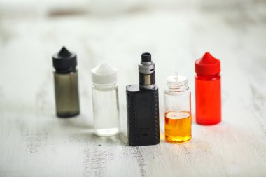 Vape nesneleri. Hafif ahşap bir masa üzerinde e-sıvı ile elektronik sigara ve kavanoz.